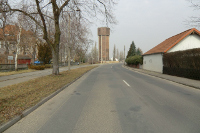 In der Bildmitte ein aus roten Klinkern erbauter Wasserturm. Eine Strasse besschreibt vor dem Turm eine Rechtskurve.